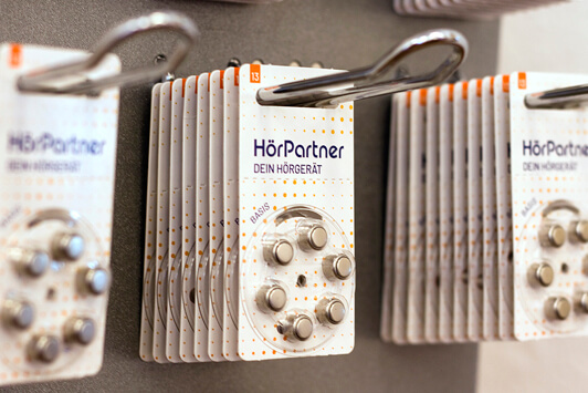 Hörgerätebatterien von HörPartner in Blisterverpackung hängen an einer Ladenwand.